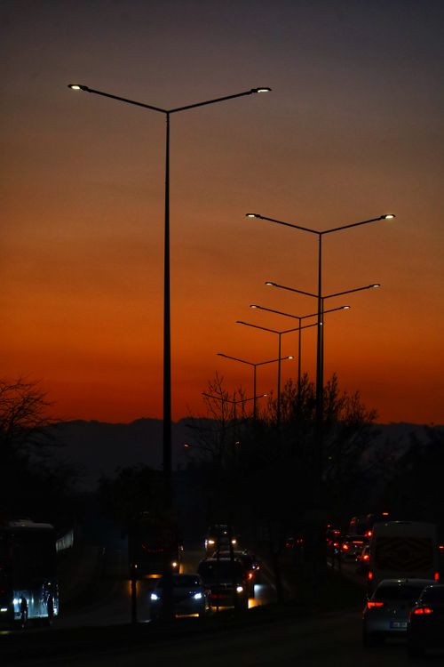 Free Cars drive under streetlights with a vibrant sunset, creating a serene urban evening scene. Stock Photo