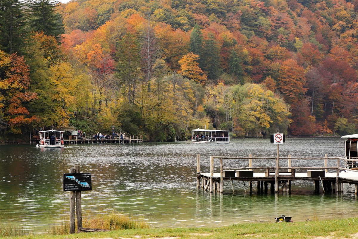 Explore the stunning autumn colors at Plitvice Lakes National Park with boats and a pier on a tranquil lake.