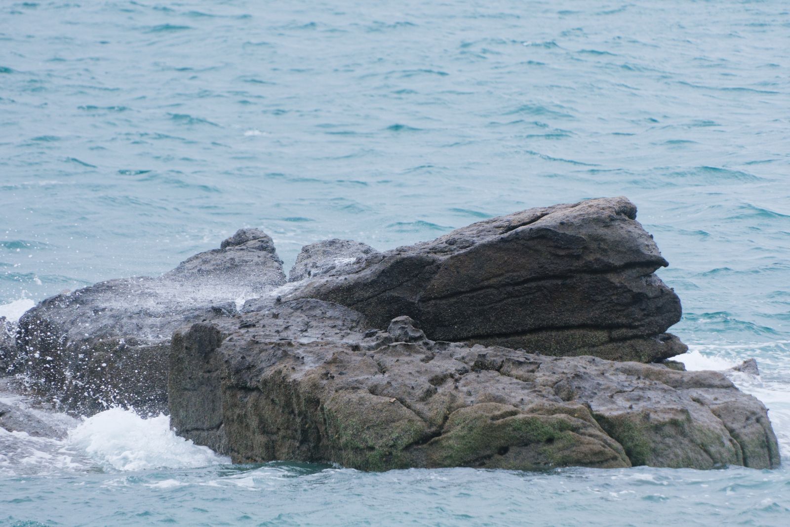Vagues éclaboussant un rocher de granit moussu dans la mer turquoise à Chausey