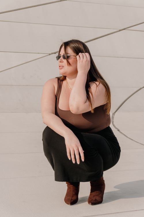 Free Fashionable woman wearing sunglasses and stylish outfit poses against a modern architectural backdrop. Stock Photo