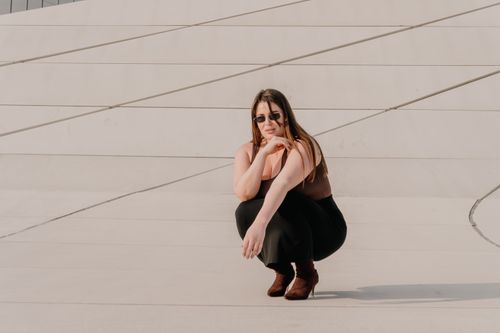 Free Fashionable woman in sunglasses squatting against a modern architectural background. Stock Photo