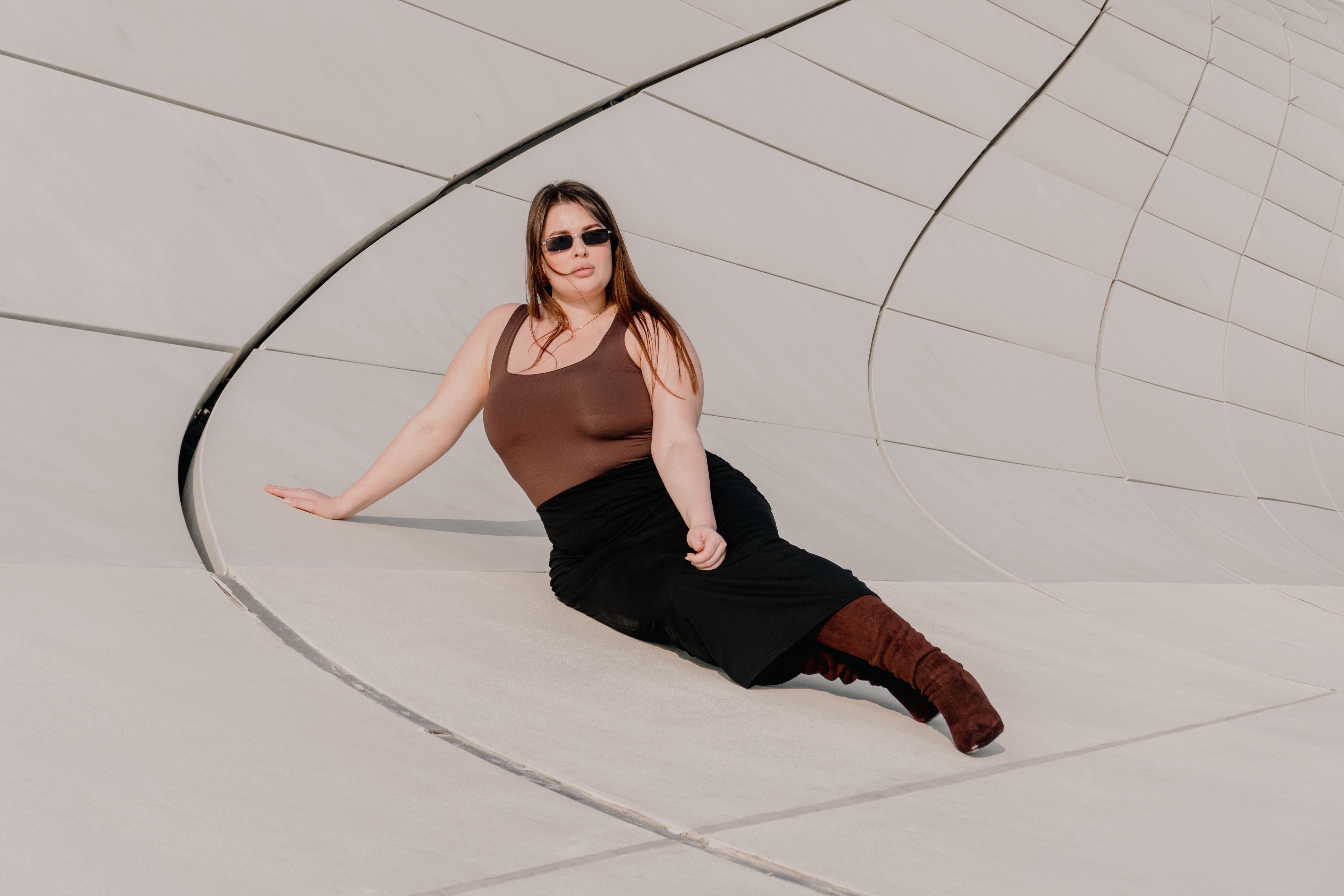 Woman in sunglasses posing against a modern architectural backdrop, exuding confidence and style.