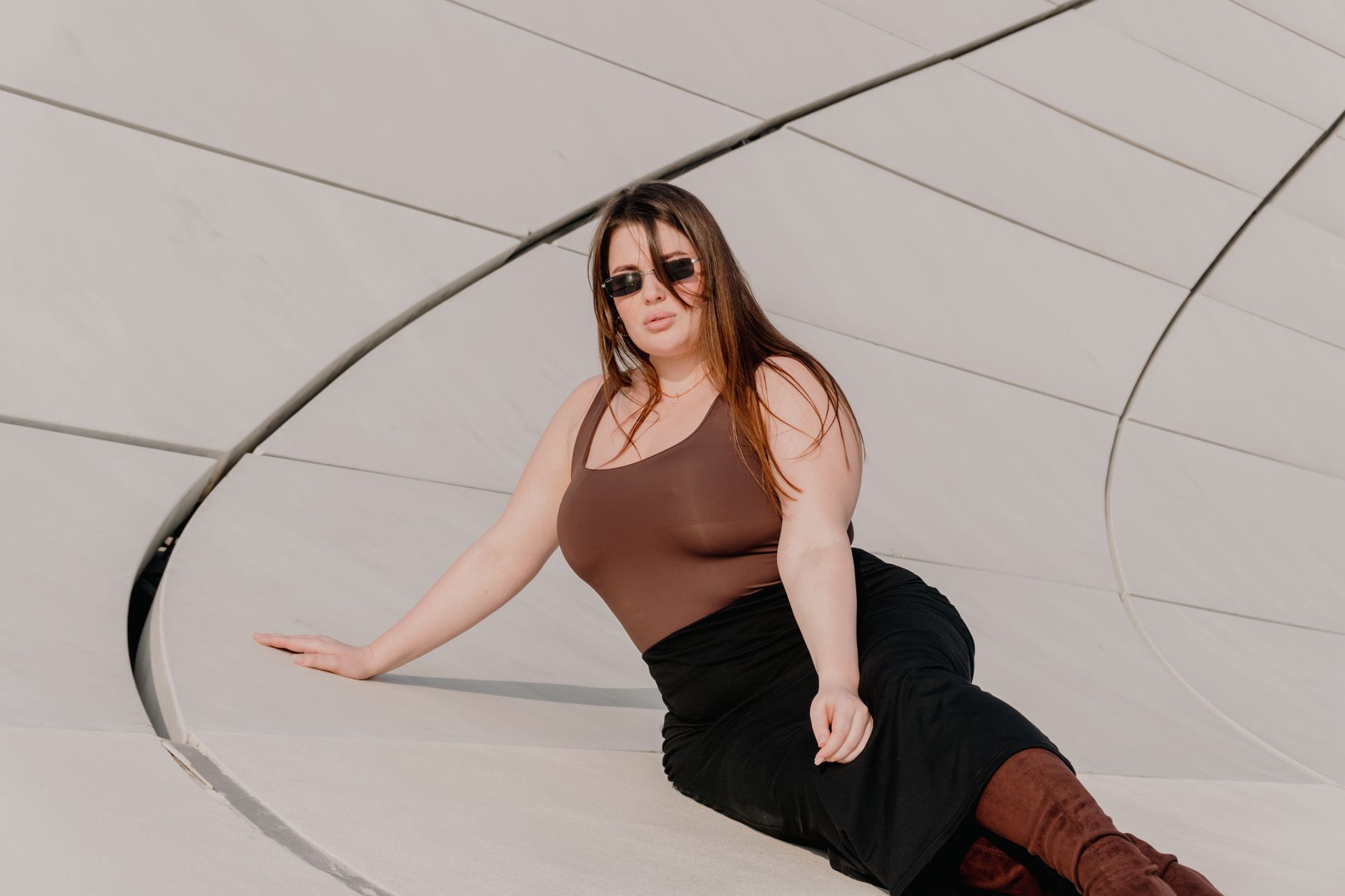 Woman in fashionable attire posing by modern architecture outdoors.