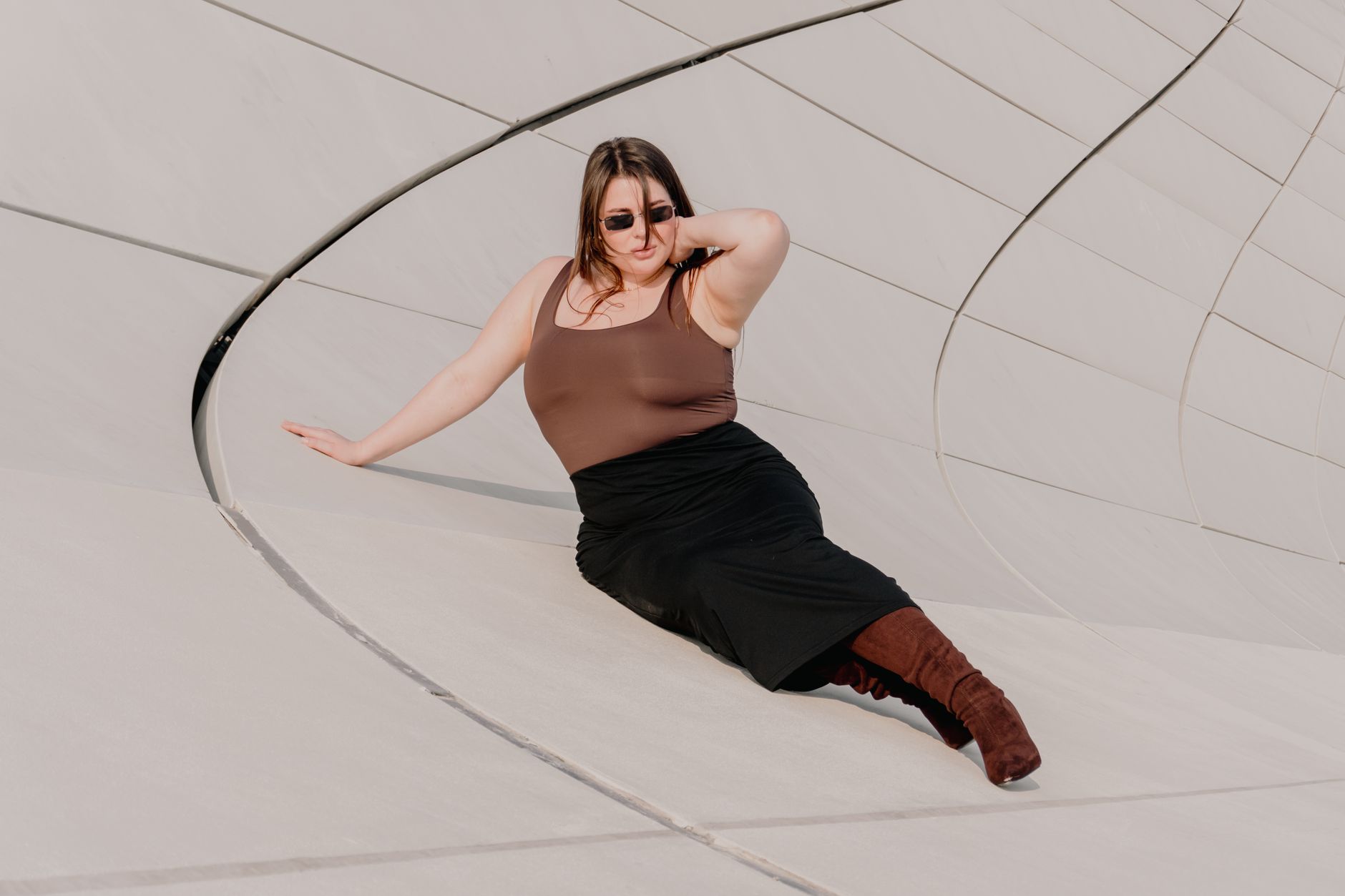 Stylish woman poses gracefully against modern architectural curves in a sunny outdoor scene.