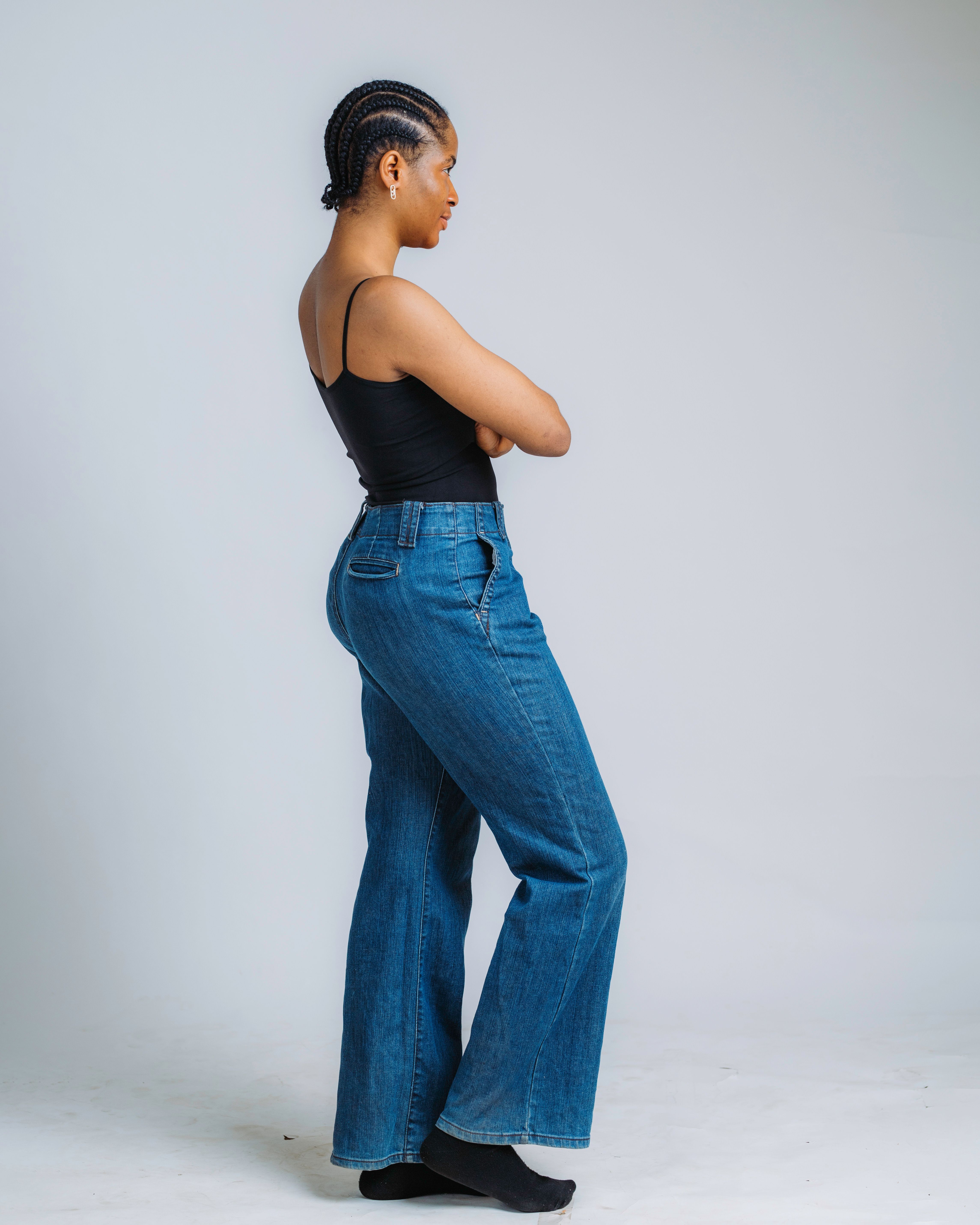 Side profile of a stylish woman in denim jeans and sleeveless top, against a neutral background.