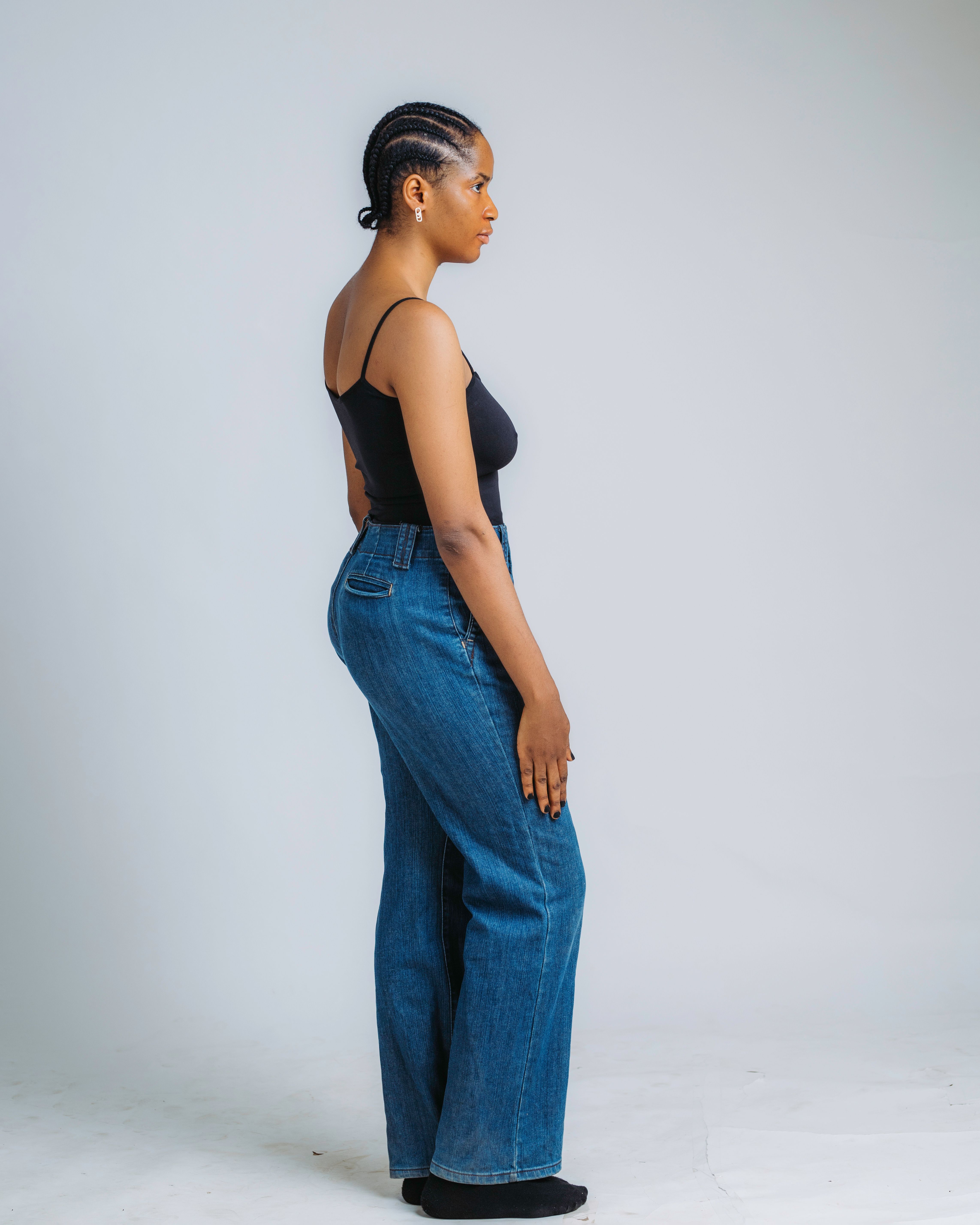 Profile portrait of a woman in a black top and jeans against a neutral background.