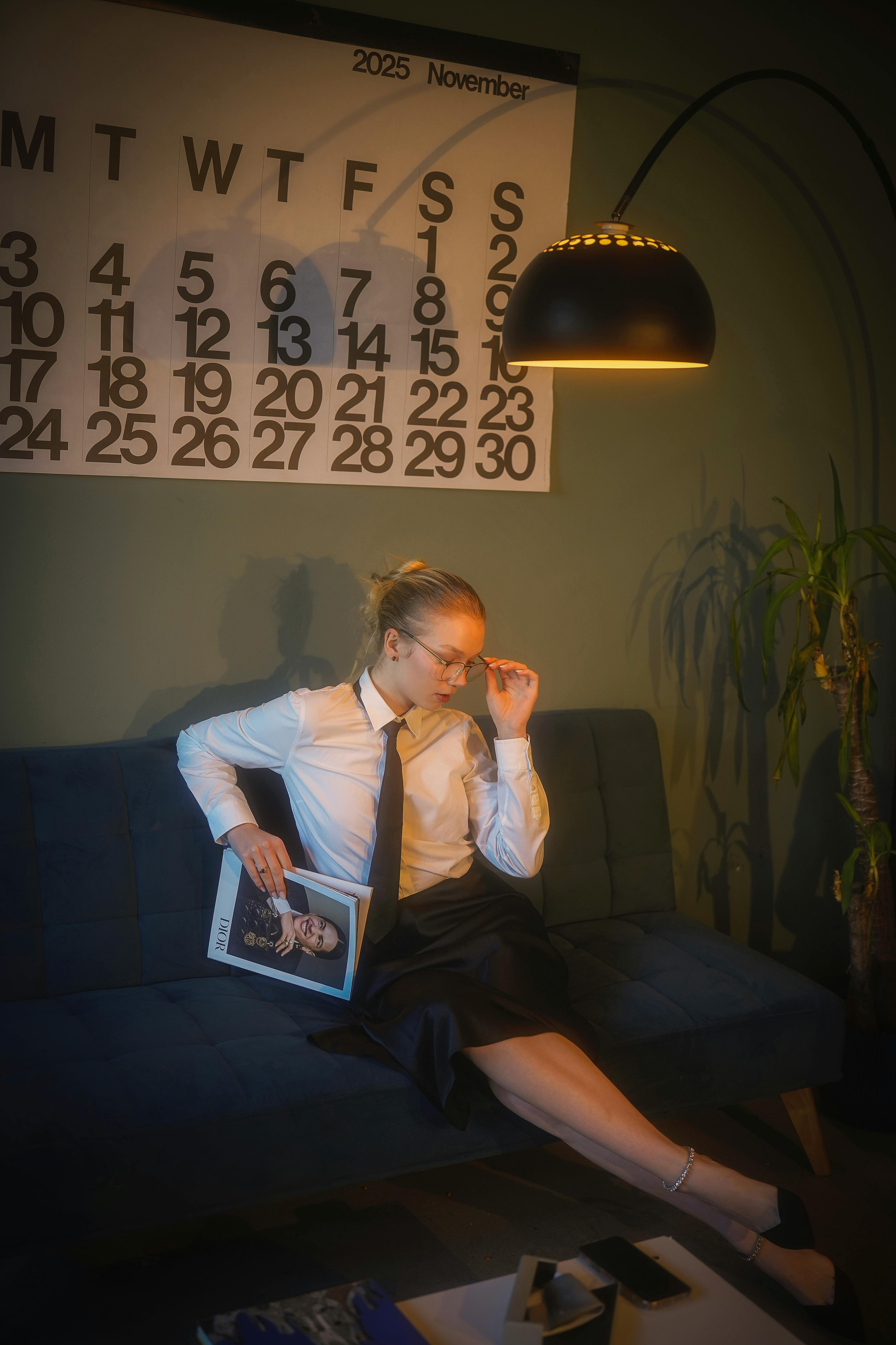 무료 따뜻한 조명 아래 소파에 앉아 잡지를 읽으며 사색에 잠긴 여성. 모던한 우아함과 고요한 사색이 어우러져 있습니다. 스톡 사진