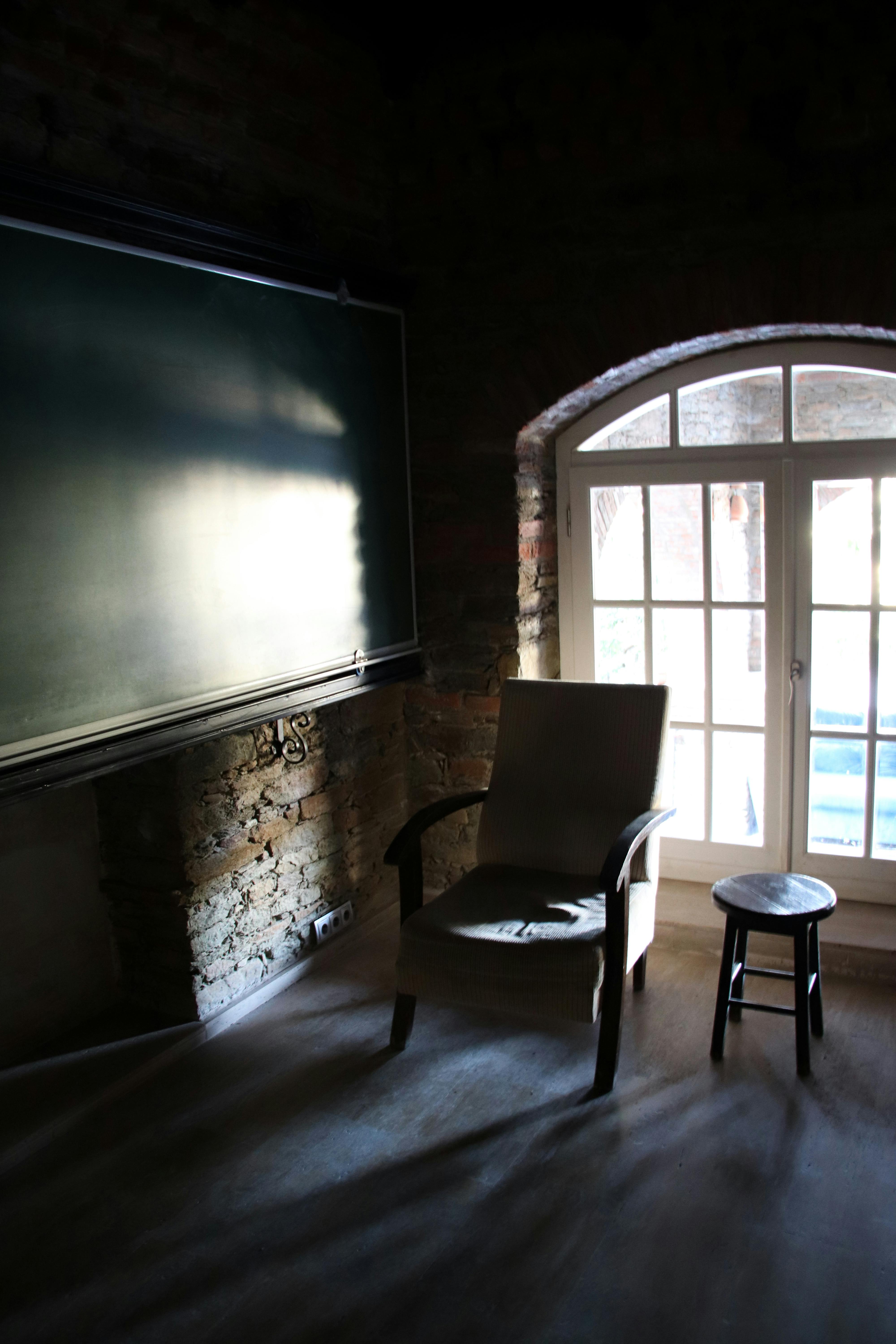 Gratuit Lumina soarelui pătrunde într-o sală de clasă istorică, dotată cu un scaun, un taburet și o tablă din lemn. Fotografie de stoc