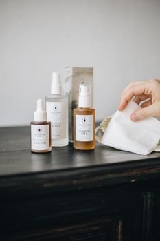 Minimalist skincare setup featuring serum, mist, and oil bottle with hand, soft light.