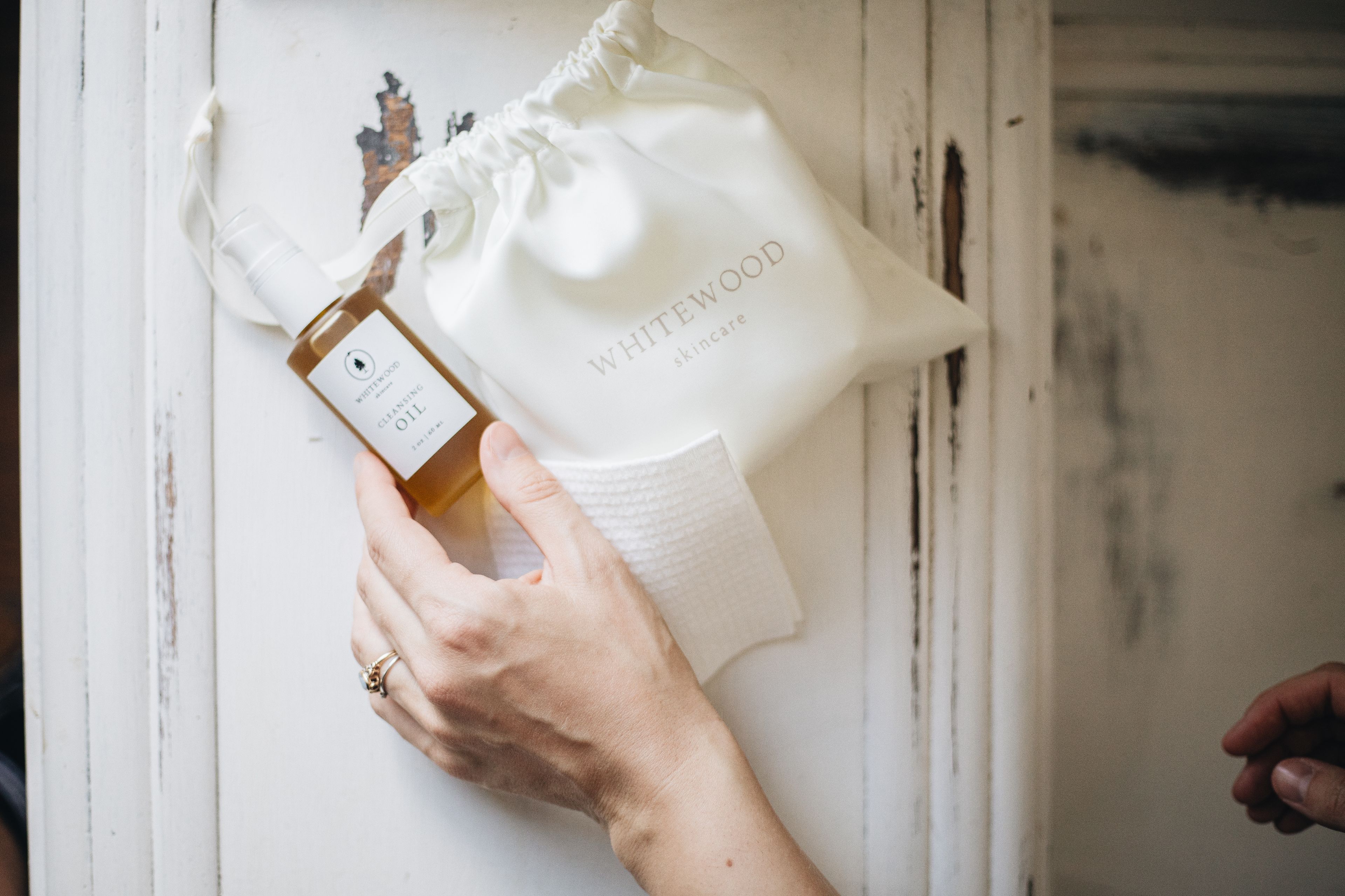 A hand lifting a cotton pouch of skincare from a shelf