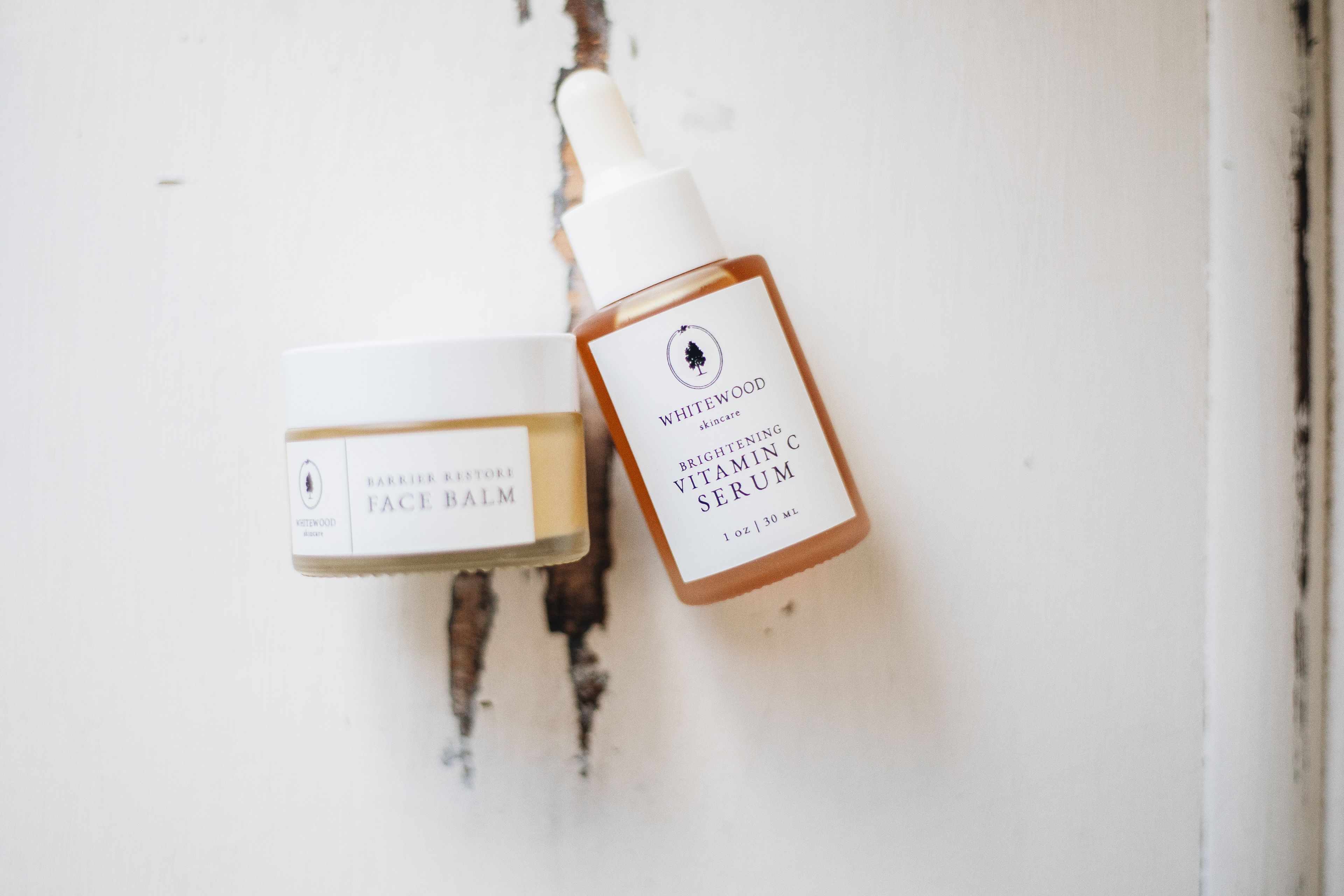 A face balm and a vitamin C serum on a pale plaster surface
