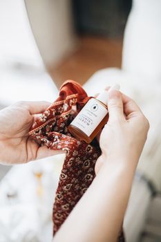 Hand holding a dropper bottle of natural skincare serum wrapped in a patterned cloth.