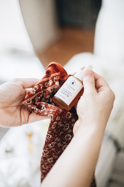 Hand holding a dropper bottle of natural skincare serum wrapped in a patterned cloth.