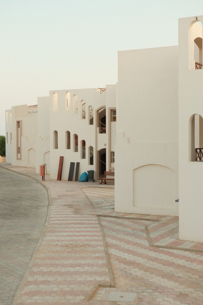 Elegant white-walled Mediterranean-style buildings along a serene street, showcasing minimalistic architecture.