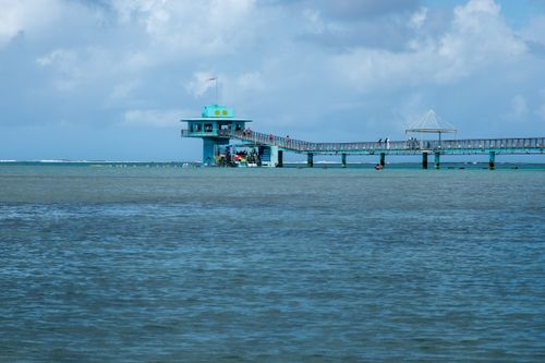 Free A beautiful turquoise structure on a pier over a calm ocean under cloudy skies. Stock Photo