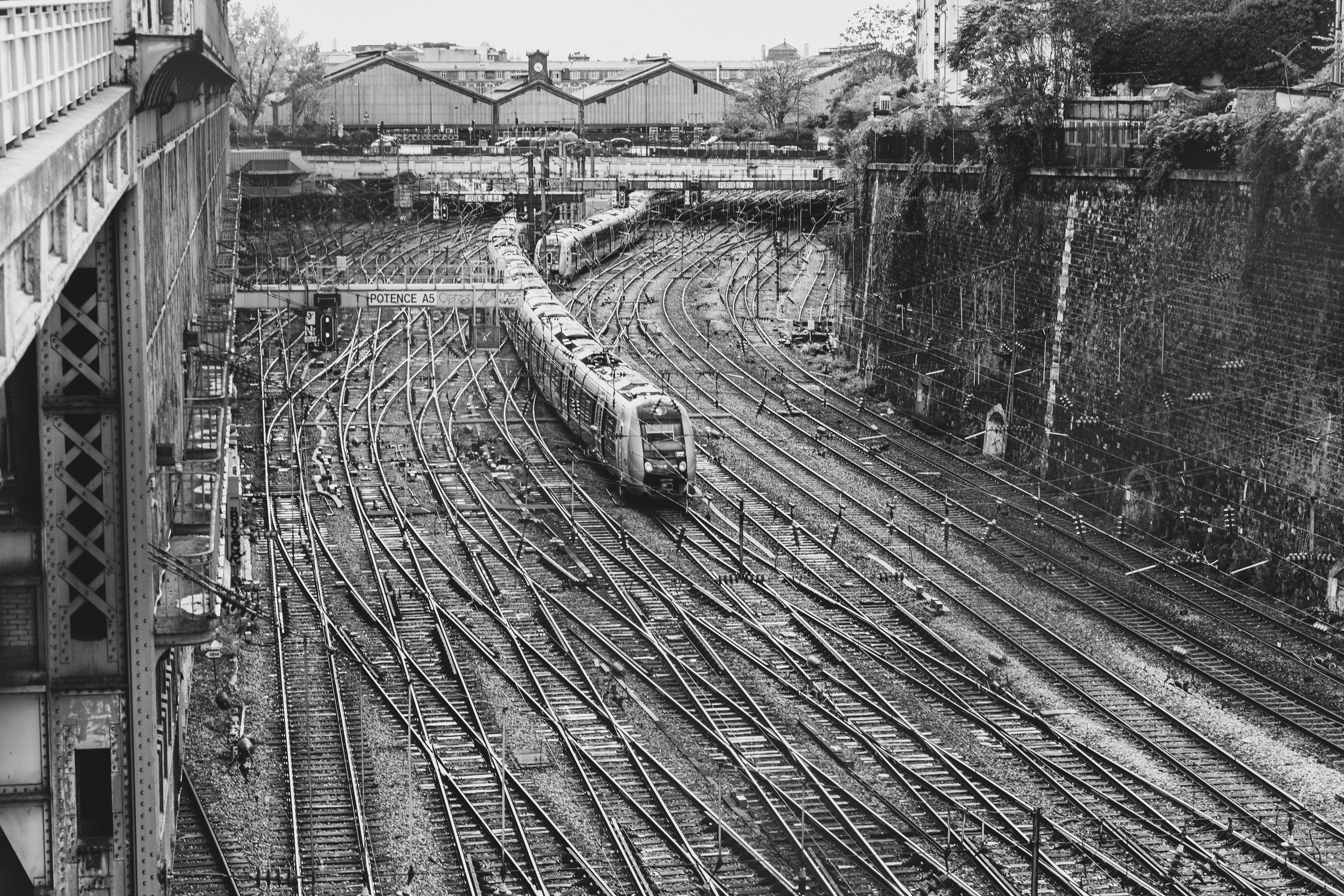 A black and white view of train tracks converging in a Paris rail yard with trains and industrial background.