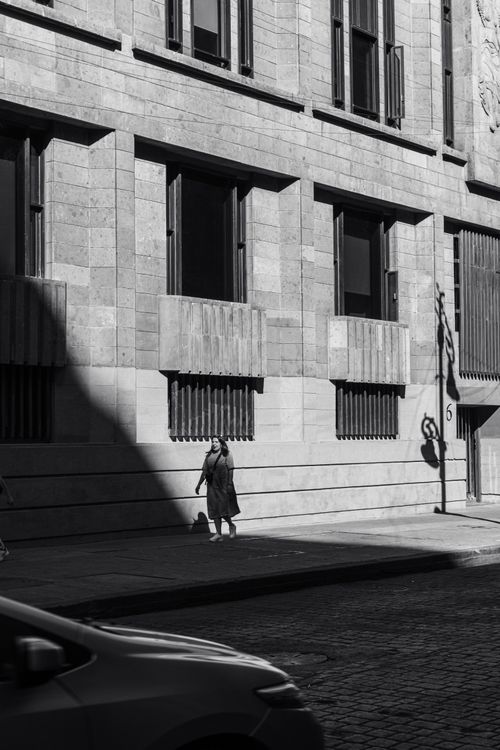 Free Monochrome photo of a city street with a pedestrian in the sunlight. Stock Photo
