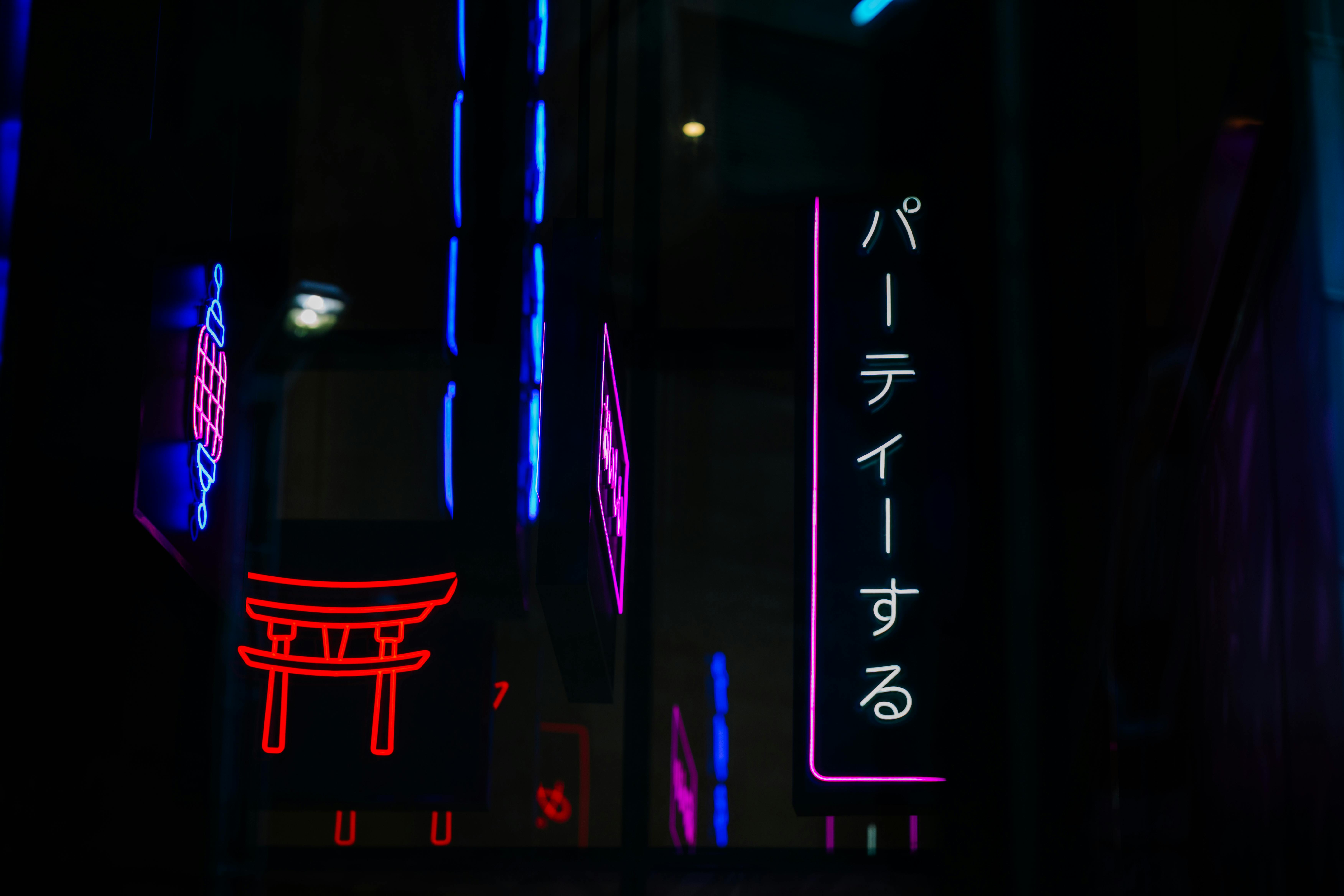 Vibrant neon signs with Japanese characters illuminate a dark urban environment, creating a colorful street scene.