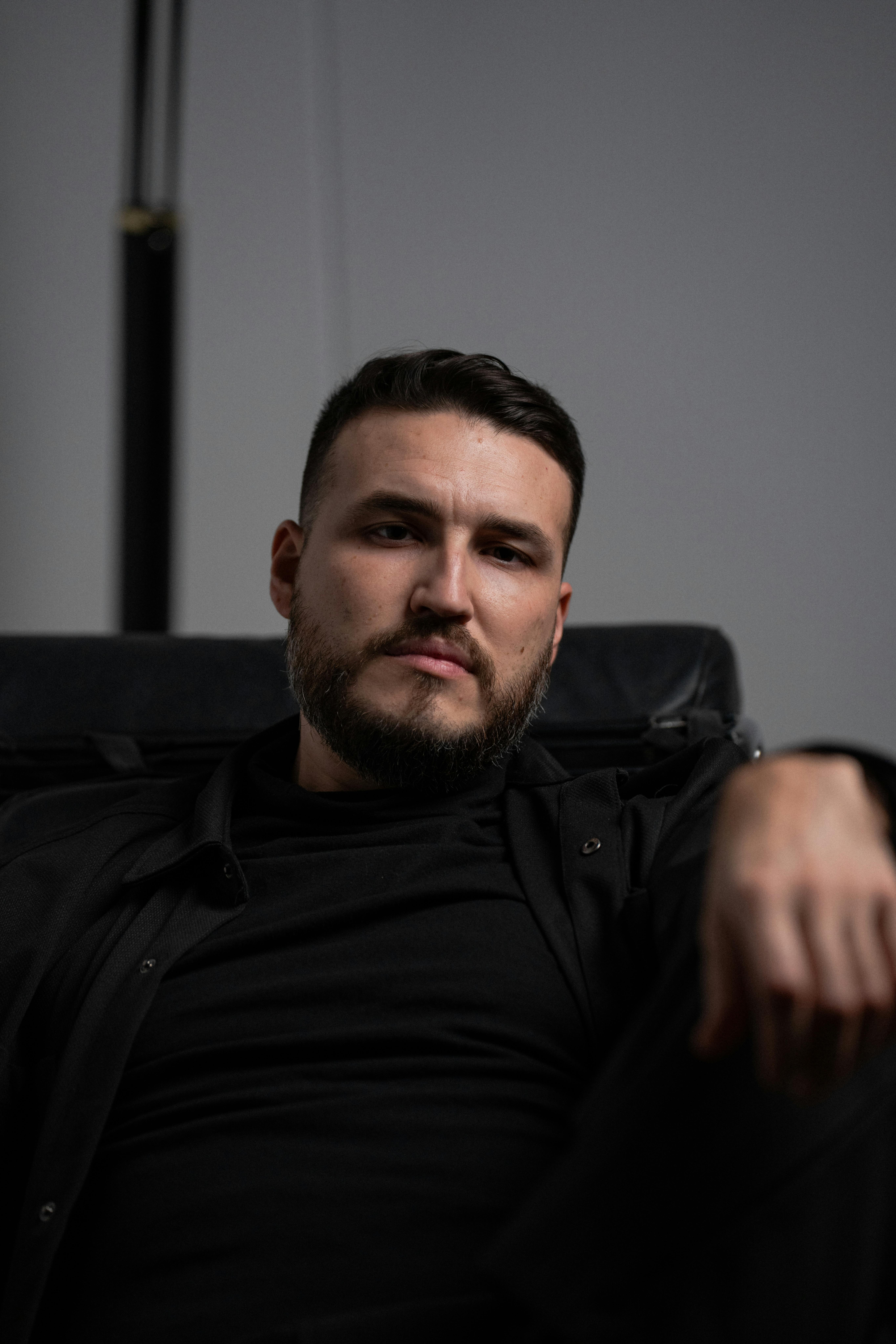 ingyenes Közeli portré egy fekete ruhás férfiról, aki elmélkedő hangulatot tükröz, beltérben. Stockfotó