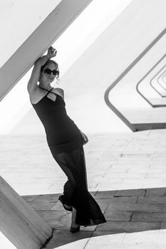 Black and white photo of a stylish woman leaning against a geometric structure.