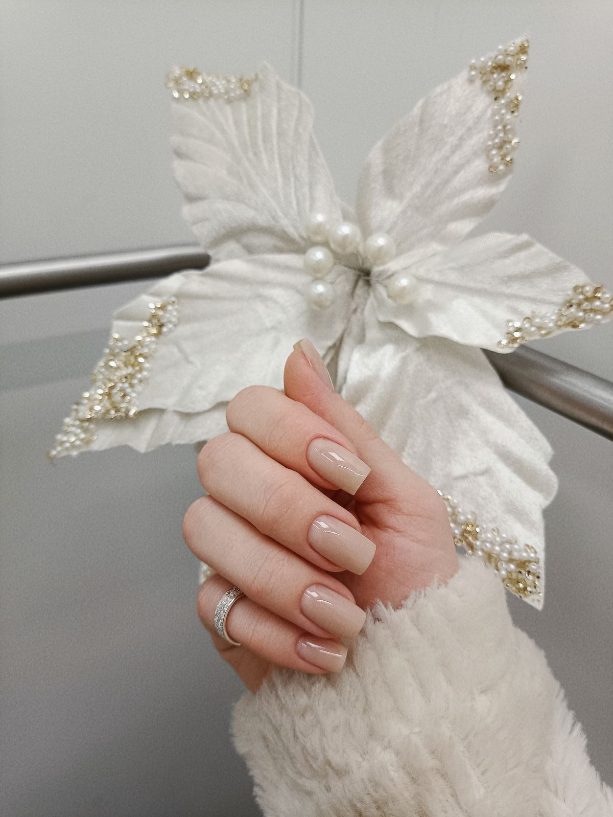 A hand with manicured nails holding a decorative white poinsettia with pearl accents.