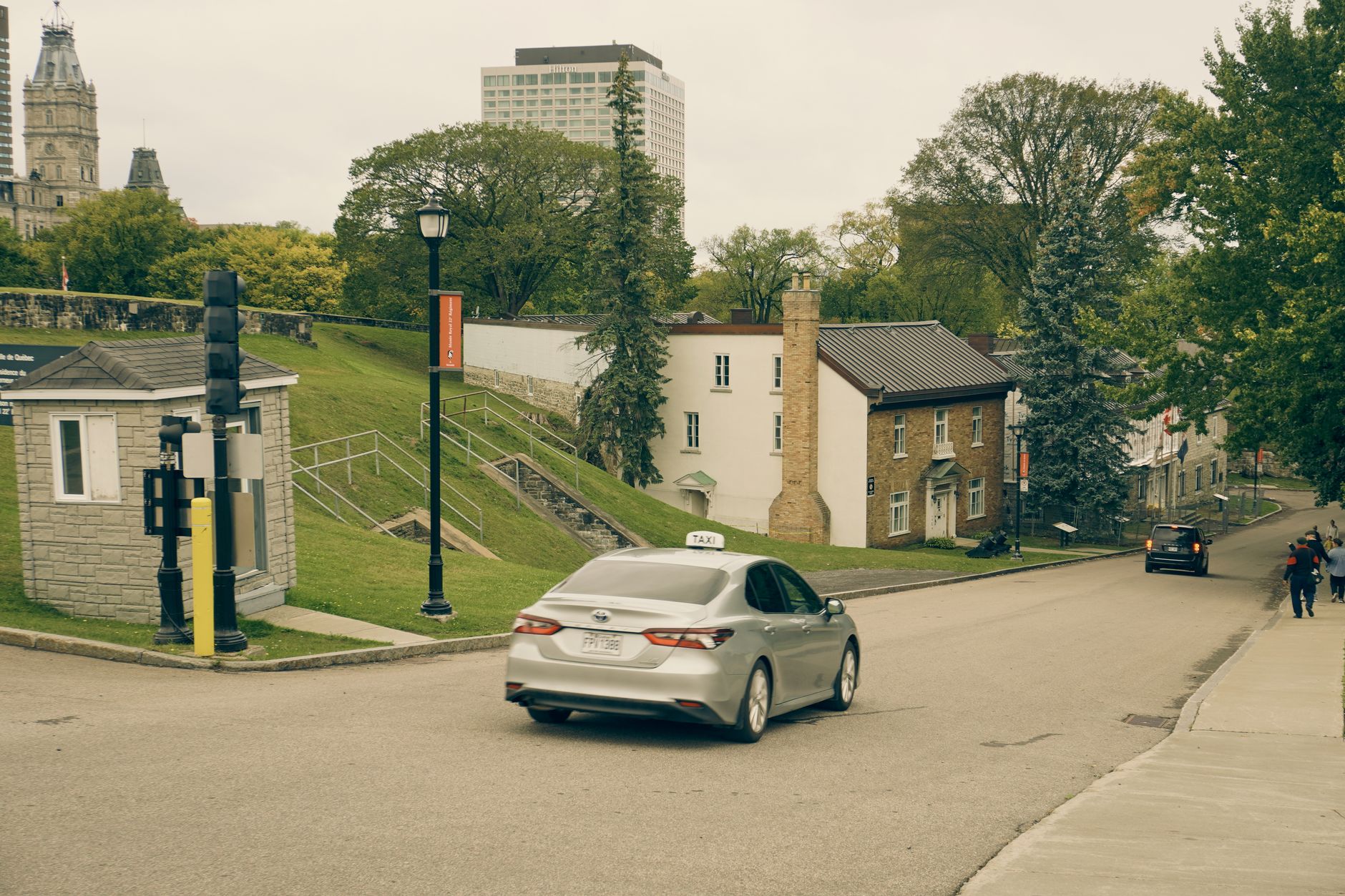 Taxi driving on a quiet street in Quebec City with historic buildings and lush trees.