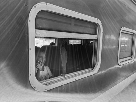 A child waves from a train window, captured in nostalgic black and white.