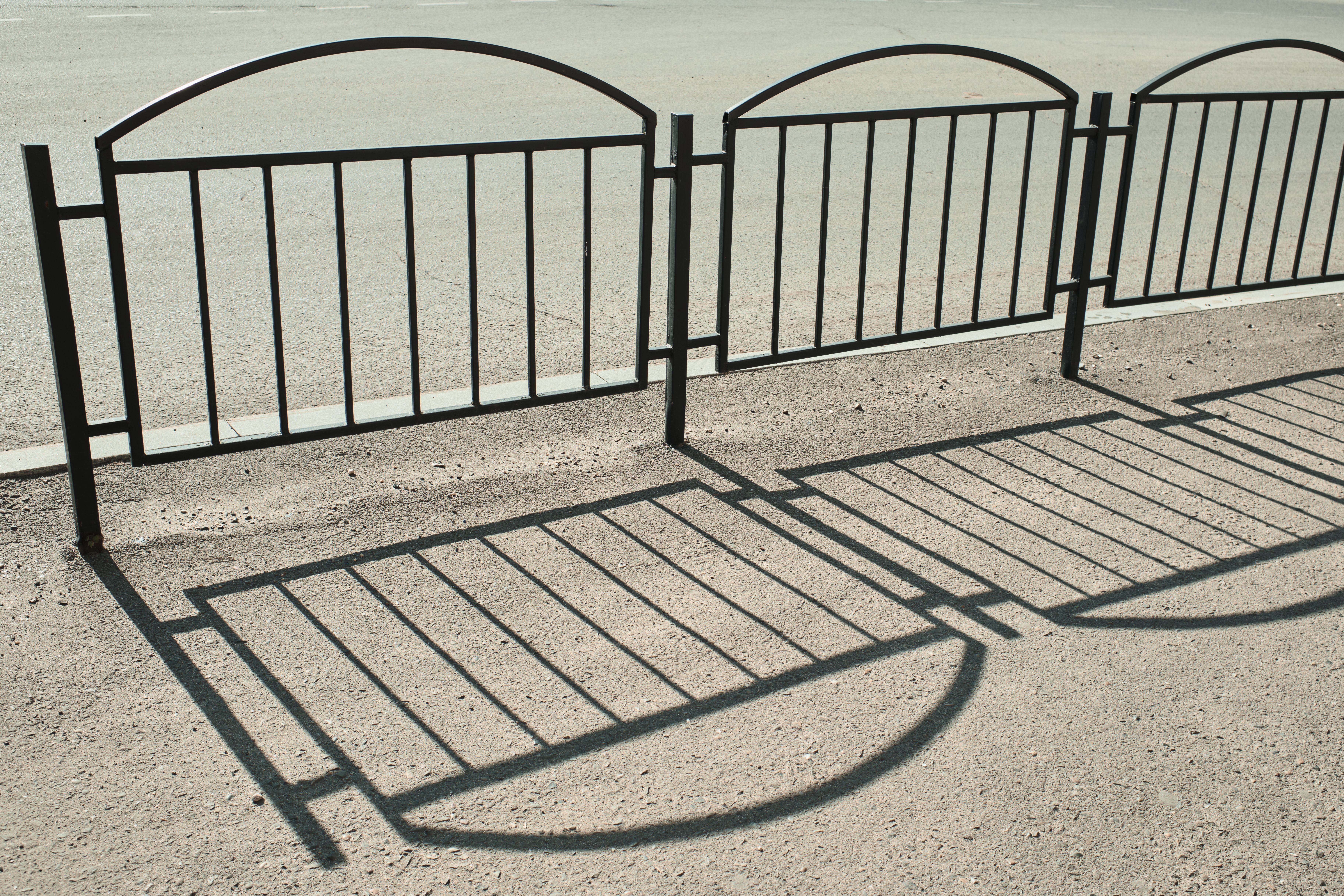Motifs d'ombres artistiques projetés par une clôture sur le trottoir sous un soleil éclatant.