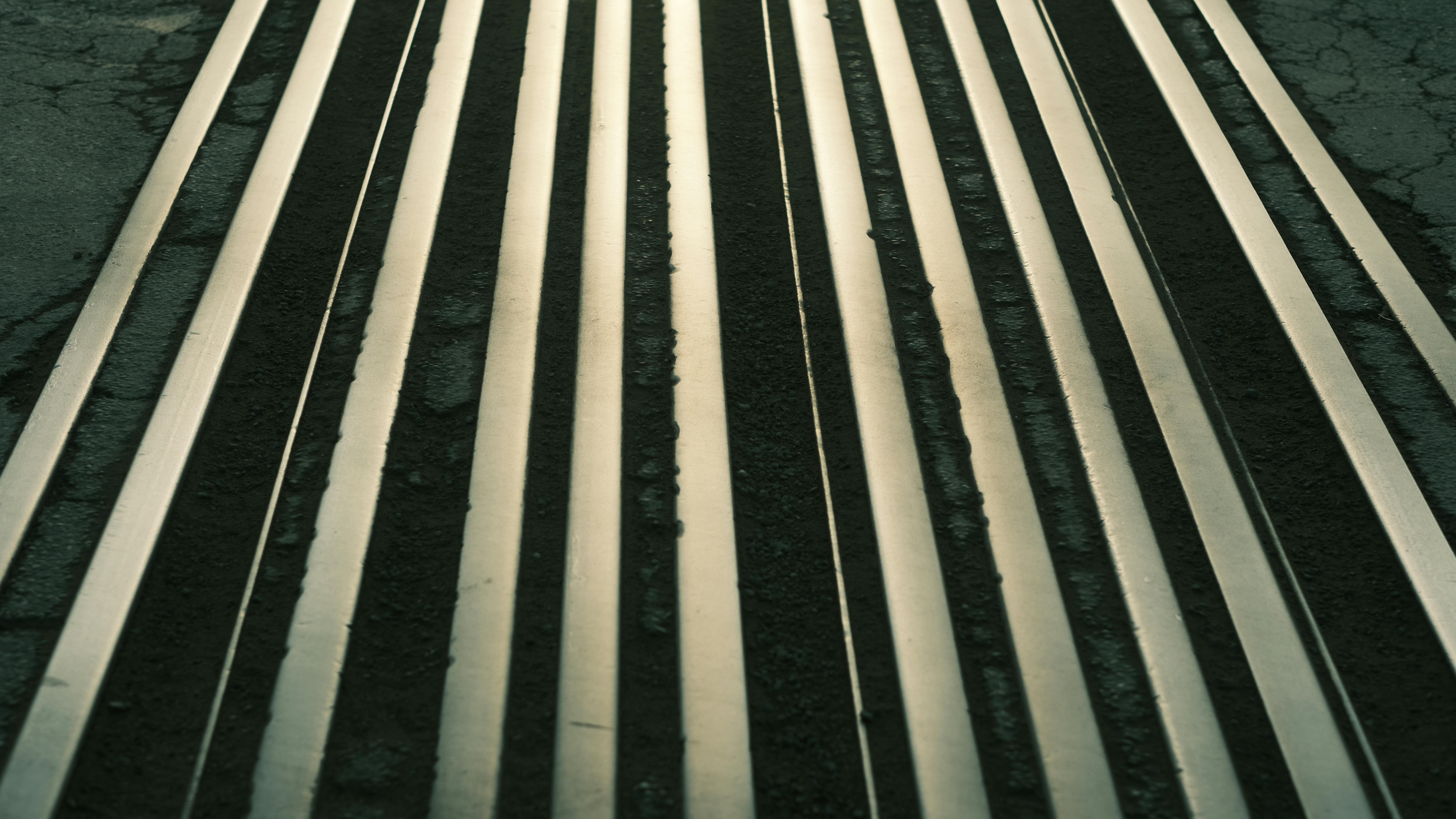 Abstract image featuring parallel metallic stripes creating a strong geometric pattern on pavement.