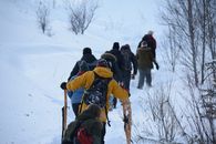 A group of people snowshoeing uphill in a snowy winter landscape.