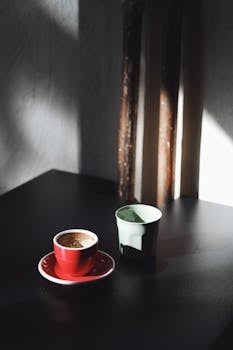 A red espresso cup on a dark table with shadows and light play.