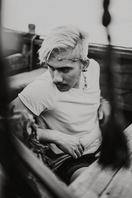 Black and white male with white dyed hair and handmade headband sitting on wooden bench resting and looking away