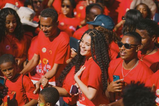 A lively crowd celebrating at an outdoor street parade wearing bright red shirts under sunny weather.