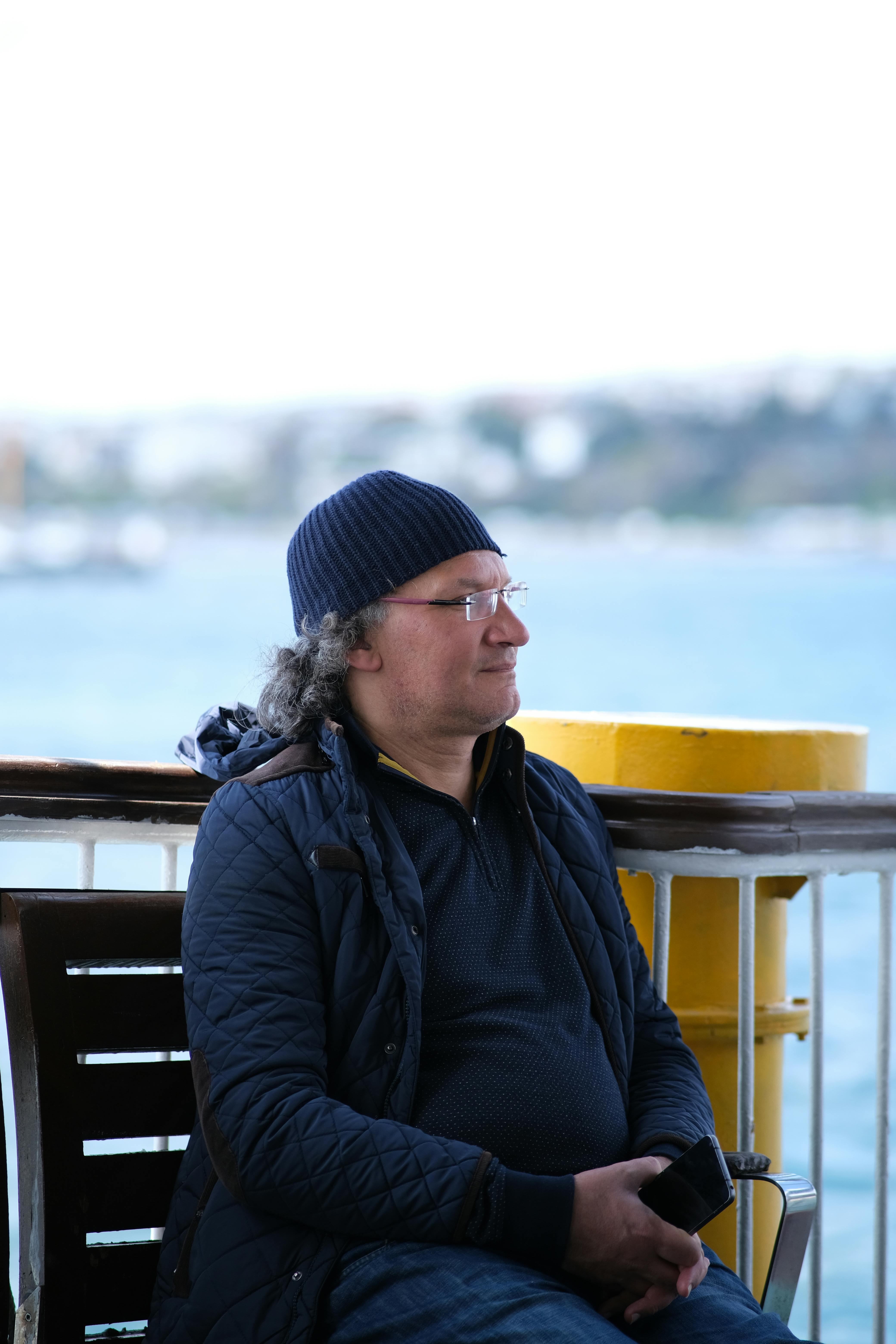 A man in winter attire relaxes on a ferry with a scenic Istanbul backdrop.