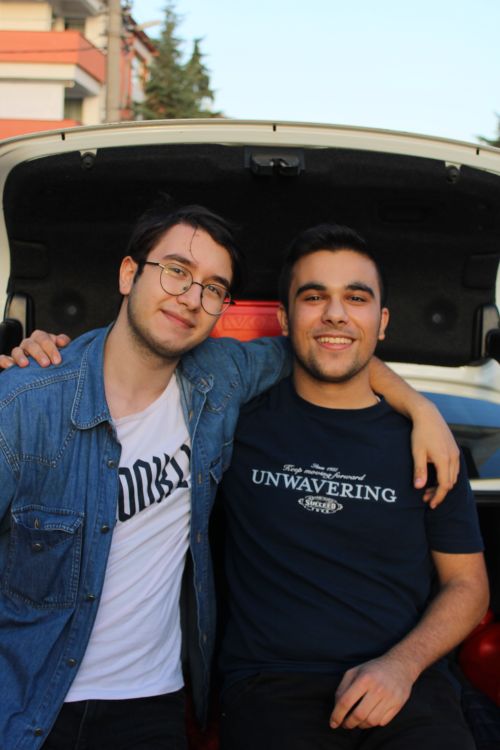Free Two young men sitting together outdoors with arms around each other, smiling and enjoying the day. Stock Photo