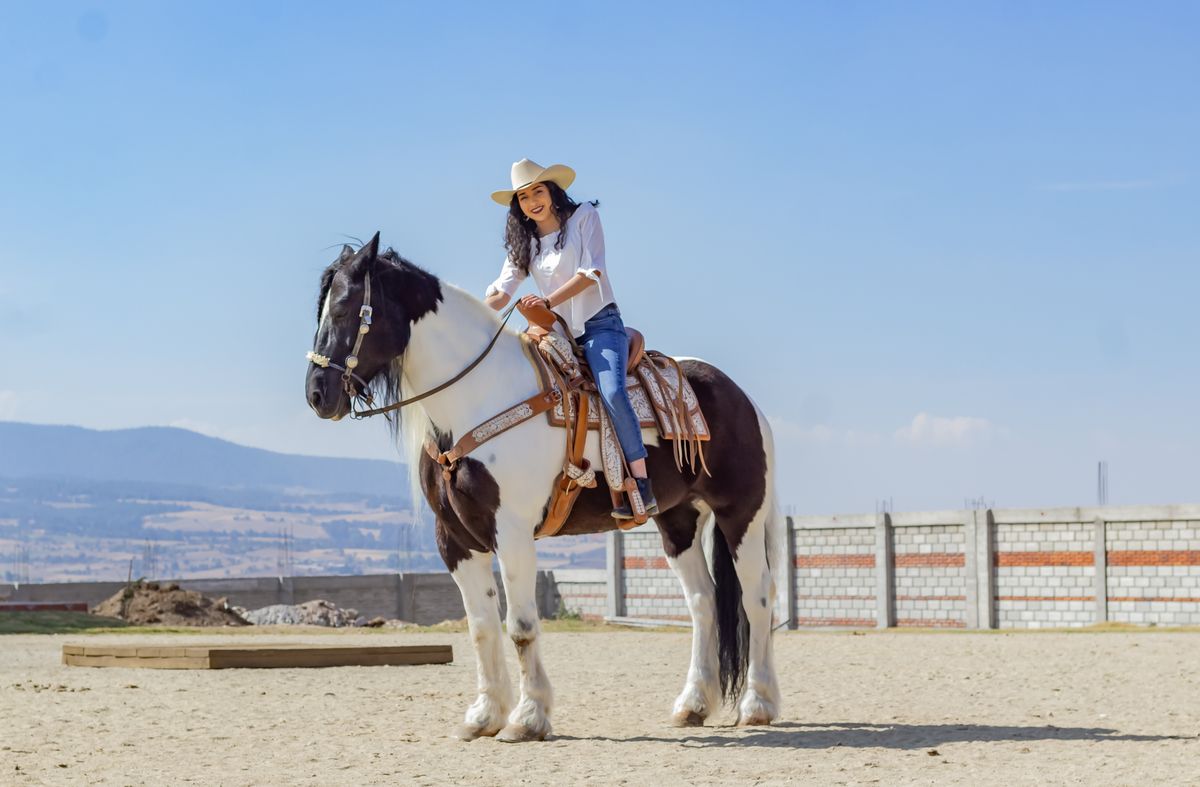 Cow-girl souriante en chapeau montant un cheval pie en plein air par une journée ensoleillée