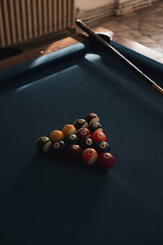 Pool table with billiard balls arranged for a game in an atmospheric indoor setting.