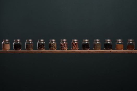 Neatly arranged spice jars on a wooden shelf against a dark background, perfect for culinary themes.