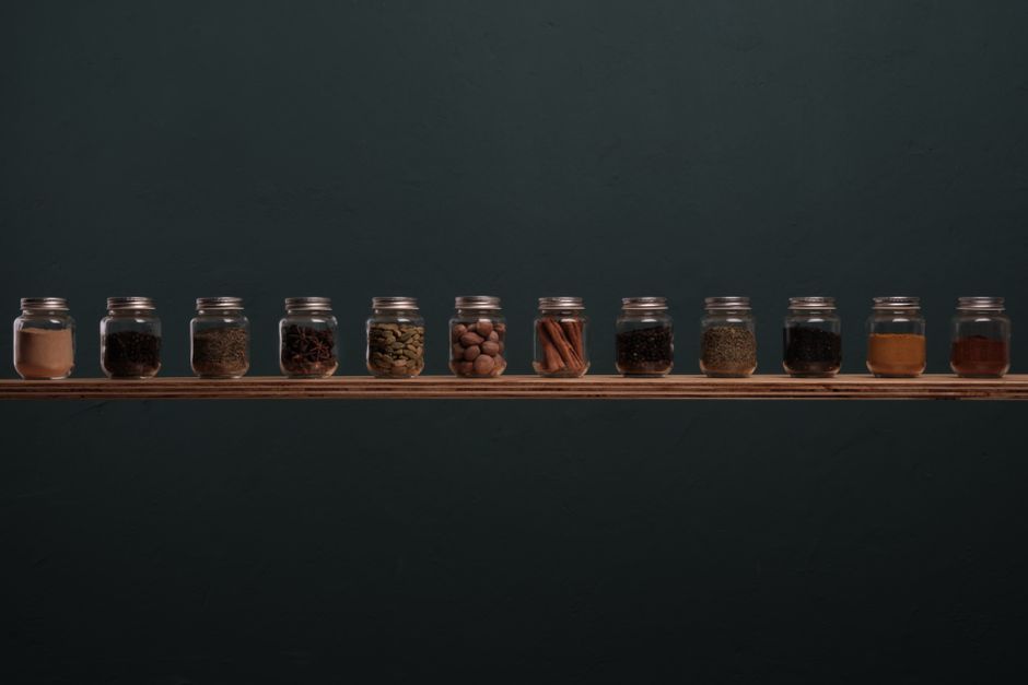 Neatly arranged spice jars on a wooden shelf against a dark background, perfect for culinary themes.