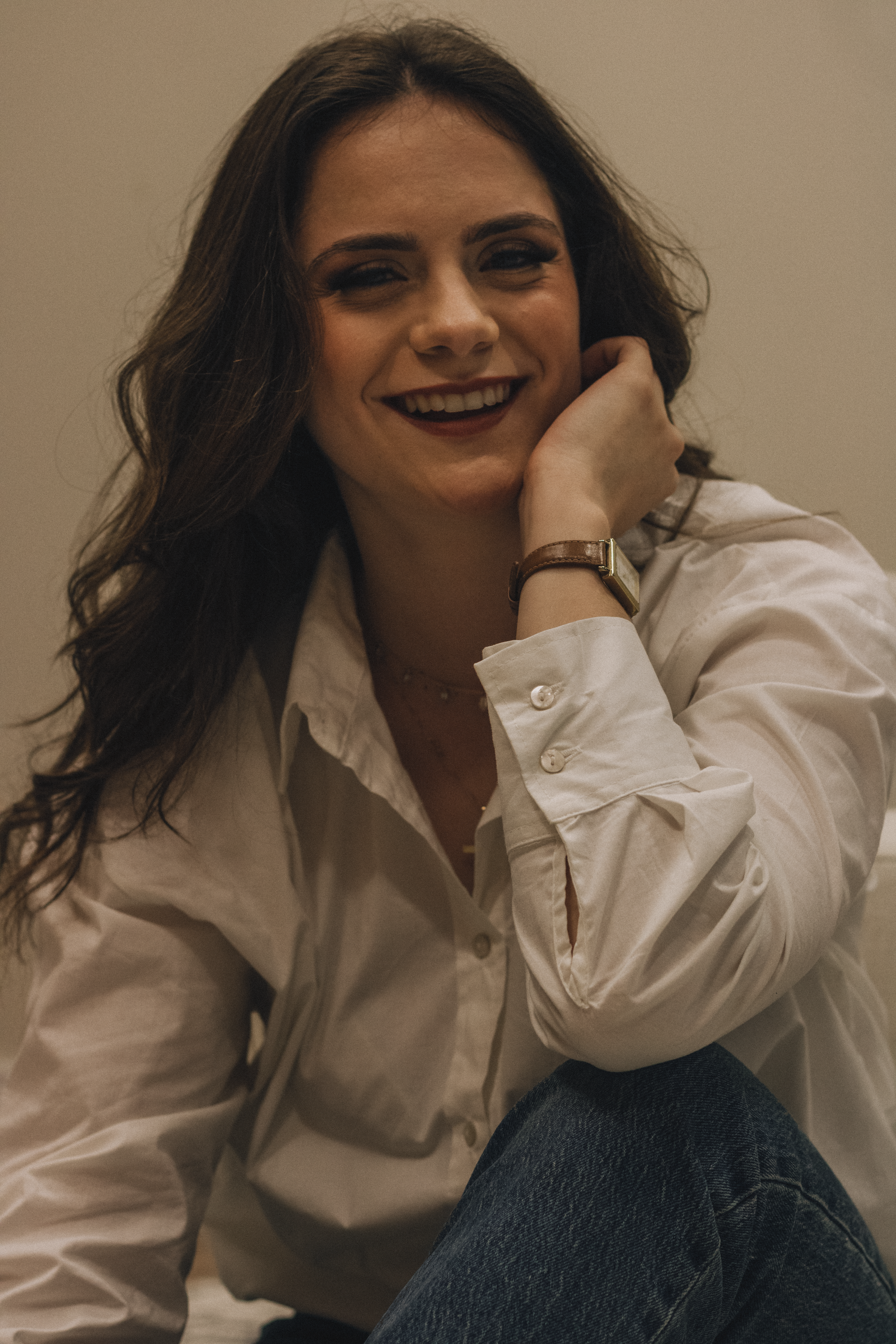 Woman in white shirt and jeans smiling while seated indoors.