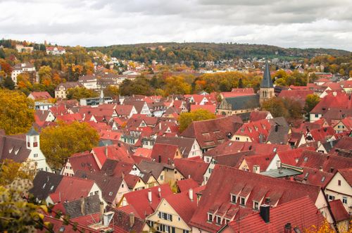 Free A picturesque aerial view of traditional German town rooftops surrounded by vibrant autumn foliage. Stock Photo