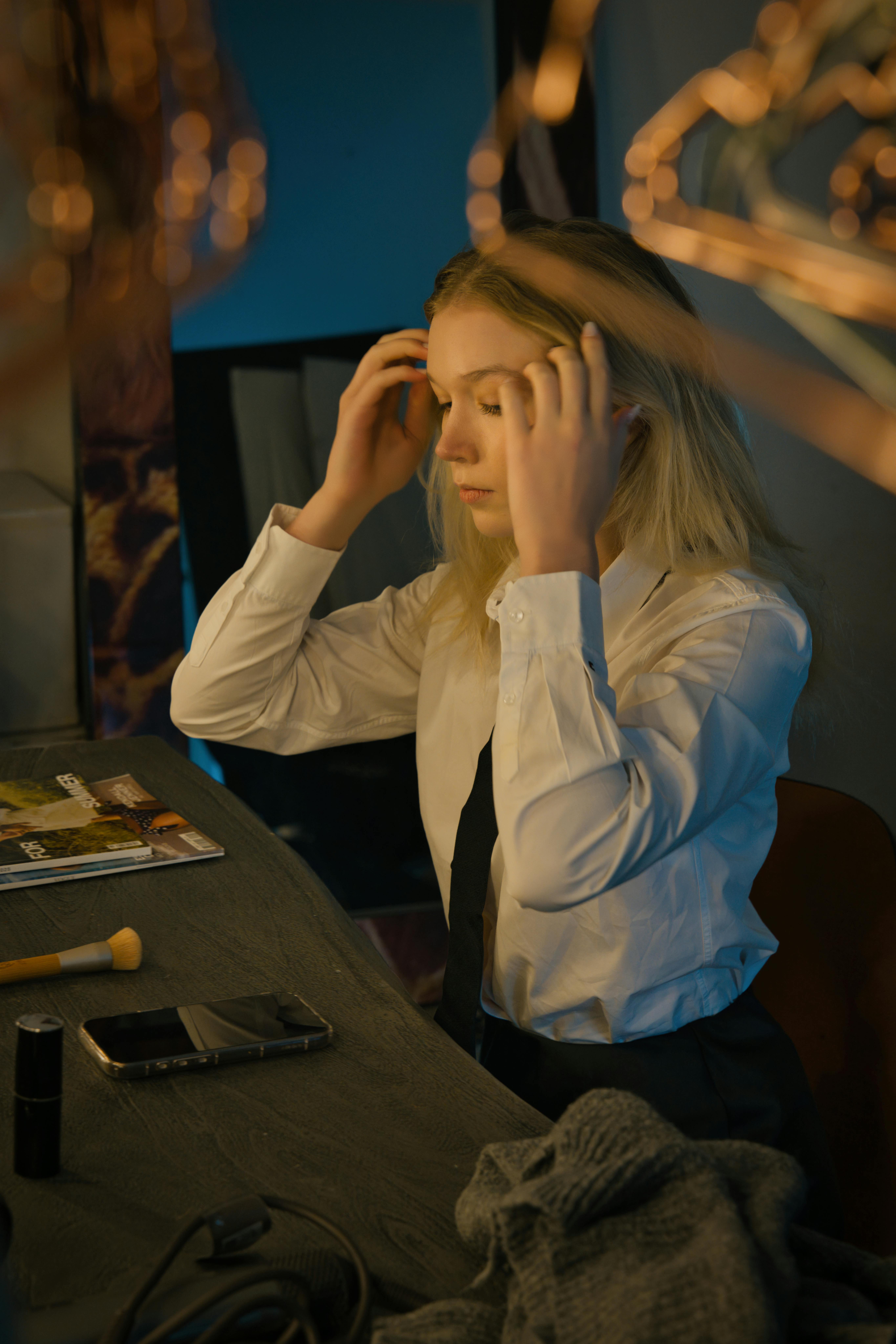 Kostenlos Junge Frau richtet sich in einer Umkleidekabine inmitten von Schminkprodukten die Haare. Stock-Foto