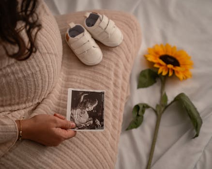 Una futura mamma tiene in mano un'ecografia con delle scarpine e un girasole, simbolo di nuovi inizi.