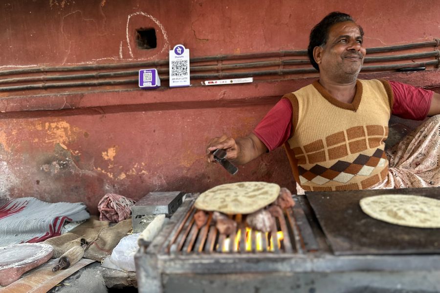 Smiling man cooking roti on open flame in a rustic street setting, India.