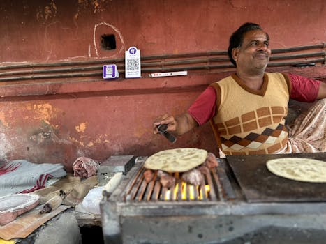 Smiling man cooking roti on open flame in a rustic street setting, India.