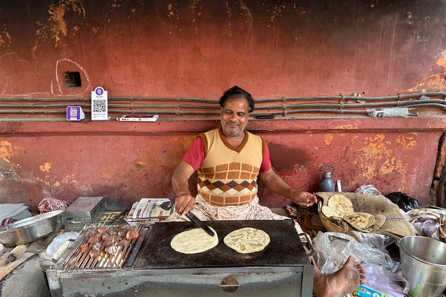 An Indian street vendor joyfully cooks traditional flatbreads on a hot griddle.