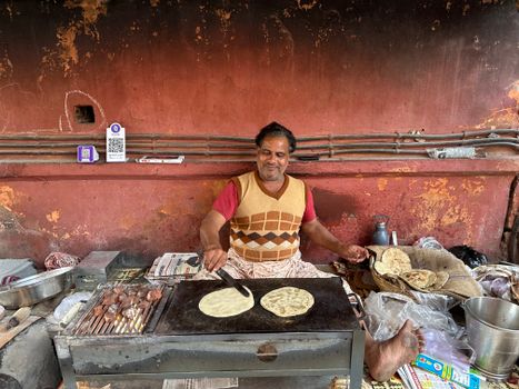 An Indian street vendor joyfully cooks traditional flatbreads on a hot griddle.