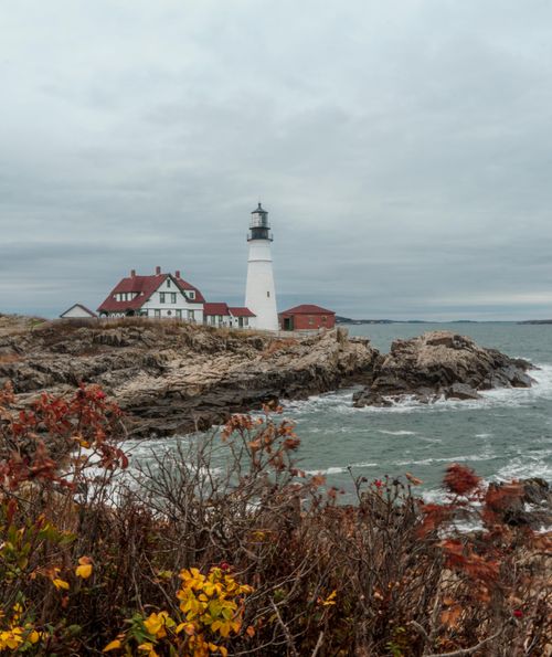 Free Scenic view of Portland Head Lighthouse on a cloudy day with rocky coastline and ocean. Stock Photo