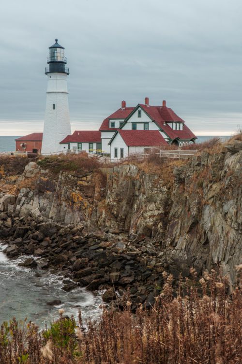 Free Iconic Portland Head Light lighthouse overlooking rocky Maine coastline under cloudy sky. Stock Photo