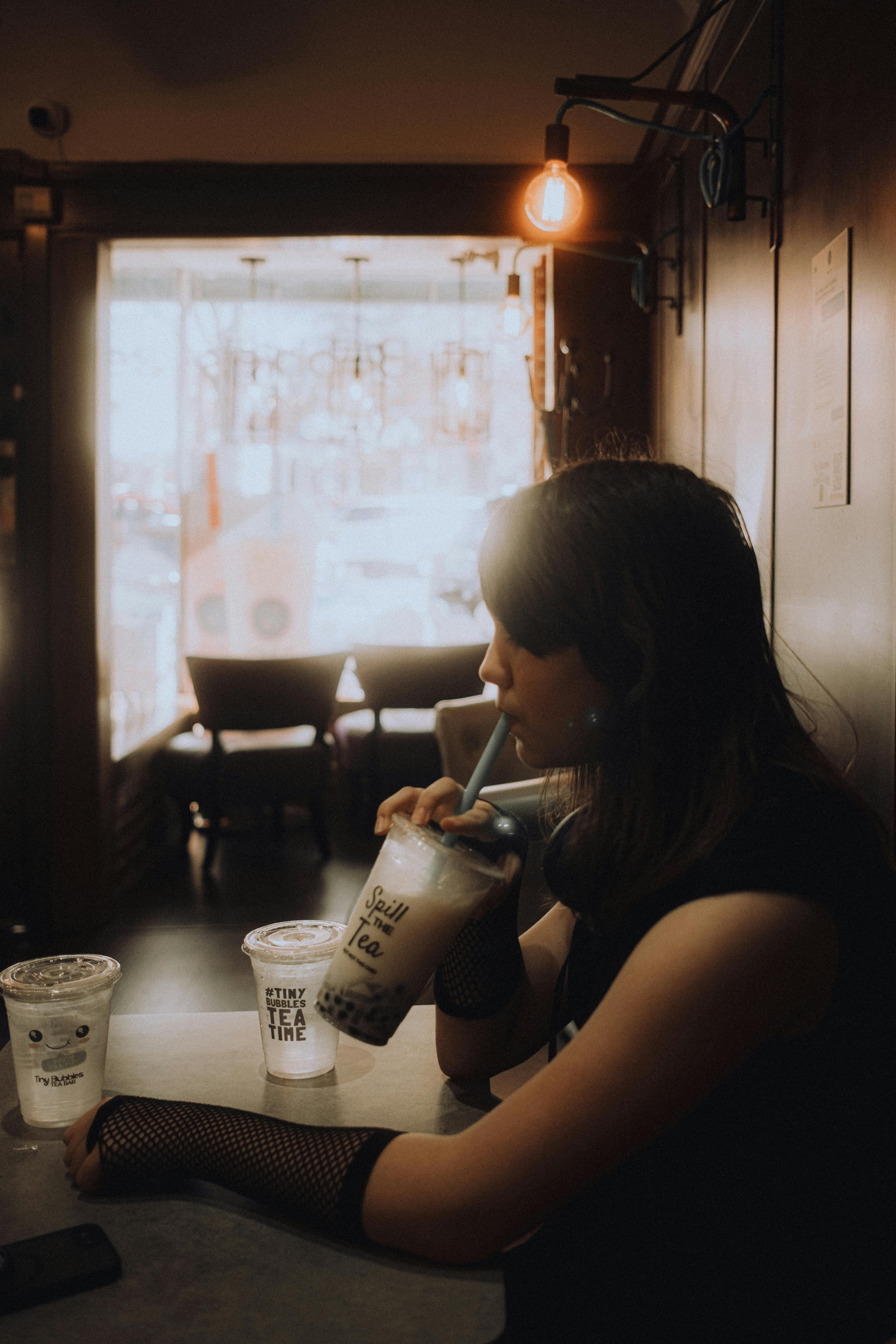 Young woman enjoying bubble tea in a cozy cafe with soft lighting and modern decor.